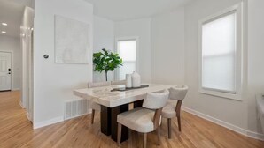 A modern dining area with a marble table, four chairs, a potted plant, and a white wall with a geometric design.
