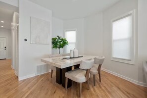 Un espace repas moderne avec une table en marbre, quatre chaises, une plante en pot et une grande fenêtre.