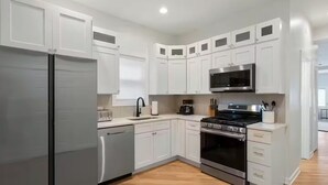 A modern kitchen with white cabinetry, stainless steel appliances, and a wooden floor.