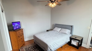 Ein Schlafzimmer mit Bett, Deckenventilator, Fernseher auf einer Holzkommode und einem gemusterten Teppich.