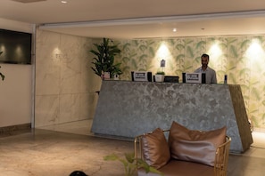 Un mostrador de recepción con una pared de mármol, una planta en maceta y un letrero que indica que no se permite el acceso a visitantes.