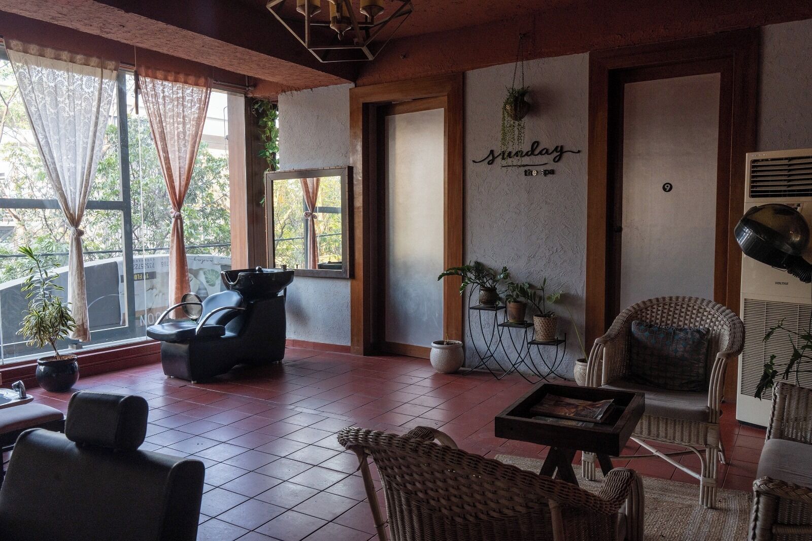 A room with a large window, a massage chair, wicker furniture, and a wall-mounted shelf with plants.
