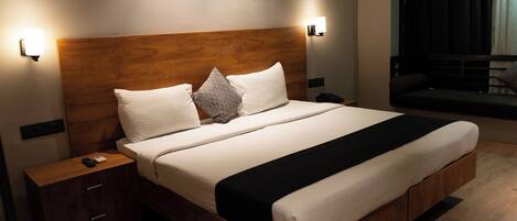 Een moderne hotelkamer met een houten hoofdeinde, een groot bed met wit beddengoed, een nachtkastje met een afstandsbediening.