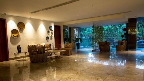 A spacious lobby with a polished marble floor, a seating area with cushioned chairs, and a large window offering a view of greenery outside. - The Elite Royale (Bengaluru)