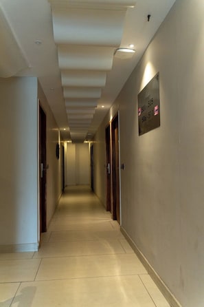 Un pasillo con puertas a ambos lados, un techo con iluminación empotrada y un cartel con números de teléfono en la pared.