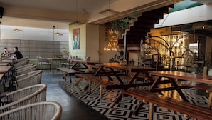 An indoor dining area with wooden tables and wicker chairs, a staircase, and a geometric patterned floor. - The Elite Royale (Bengaluru)