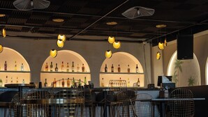 A bar area with arched shelving, hanging pendant lights, and metal chairs. - The Elite Royale (Bengaluru)