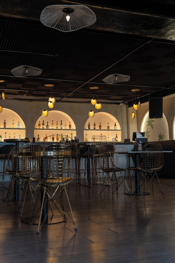 Un área de bar con estanterías de arco, luces colgantes y sillas de metal.