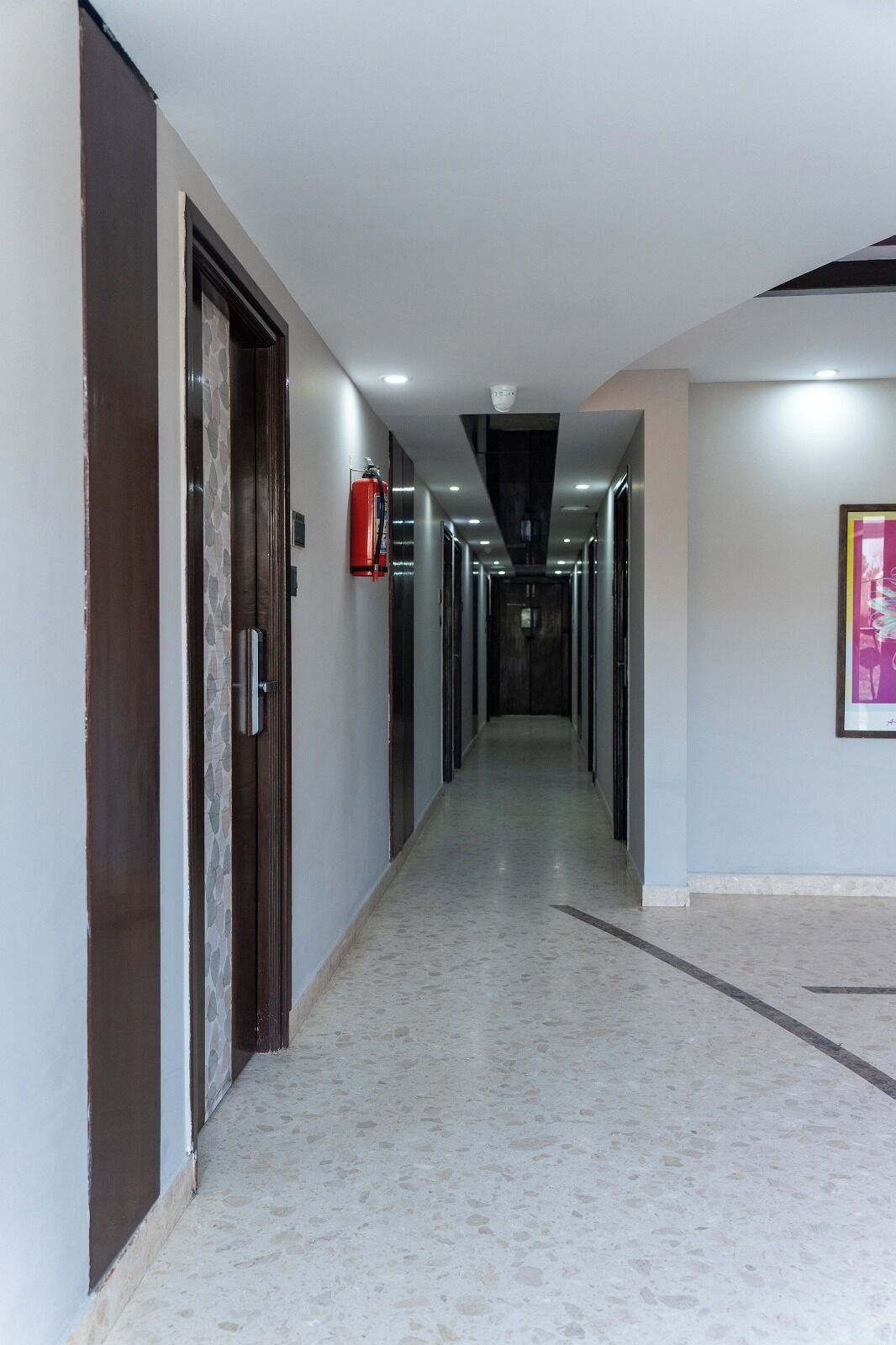 A long, narrow hallway with doors on both sides, a fire extinguisher mounted on the wall, and a ceiling light.
