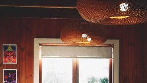 A wooden interior with a table and chairs, a hanging light fixture, and a window with a view of greenery. - Casa del Estero in downtown Pucón (Pucon)