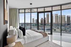 Ein modernes Schlafzimmer mit einem großen Bett, Blick auf eine Stadtlandschaft durch raumhohe Fenster und einer minimalistischen Einrichtung.