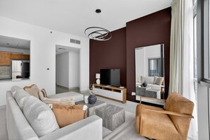 A modern living room with a sofa, ottoman, and armchair, a flat-screen TV, and a large mirror. - Silkhaus Modern 2bdr Flat in Julphar Tower (Abu Dhabi)