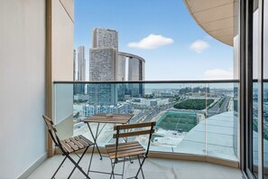A balcony with two wooden chairs and a table, overlooking a cityscape with modern buildings and a clear sky. - Silkhaus Modern 2bdr Flat in Julphar Tower (Abu Dhabi)