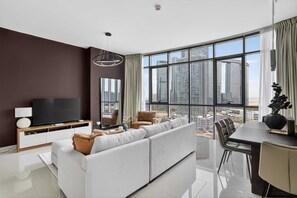 A modern living room with a large window, a flat-screen TV, a sofa, a dining table, and chairs. - Silkhaus Modern 2bdr Flat in Julphar Tower (Abu Dhabi)
