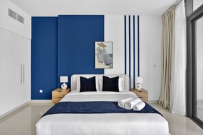 A modern hotel room with a large bed, bedside tables, a painting, and a view of the outdoors. - Silkhaus Modern 2bdr Flat in Julphar Tower (Abu Dhabi)