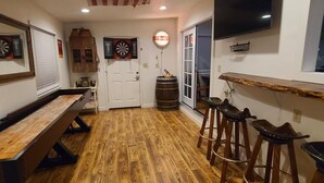 Une pièce équipée d’un jeu de fléchettes, d’un plancher en bois, d’un coin bar avec des tabourets et d’un téléviseur fixé au mur.