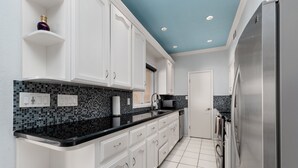 A kitchen with white cabinets, a black countertop, and a stainless steel refrigerator. - Ground floor Madre walk out w/boat slip! (South Padre Island)