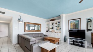 A living room with a sectional sofa, a coffee table, a TV on a stand, and a shelving unit with decorative items. - Ground floor Madre walk out w/boat slip! (South Padre Island)