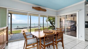 A dining area with a view of the ocean, a ceiling fan, and a large window. - Ground floor Madre walk out w/boat slip! (South Padre Island)