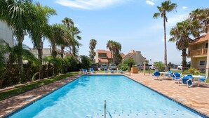 A swimming pool with a clear blue water, surrounded by palm trees and lounge chairs. - Ground floor Madre walk out w/boat slip! (South Padre Island)