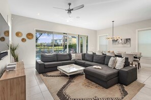 A modern living room with a sectional sofa, a coffee table, and a dining area with a chandelier.