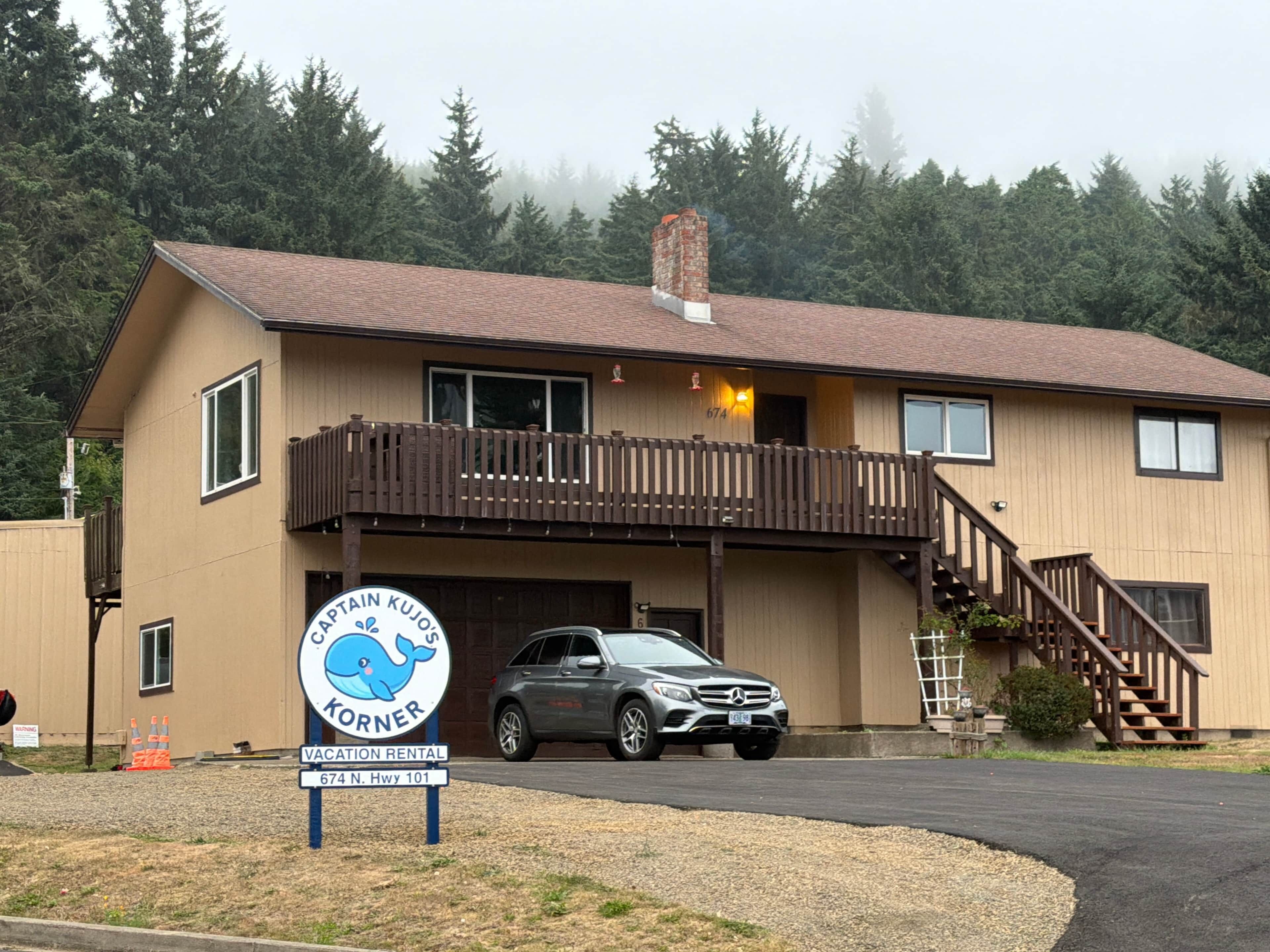 A two-story building with a wooden deck and a car parked in front.