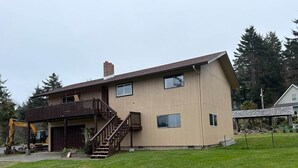 A two-story building with a balcony, a staircase, and a construction vehicle nearby. - Captain Kujo’s Hideaway (Depoe Bay)