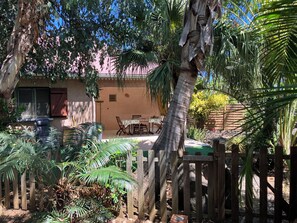 A patio with a table and chairs, surrounded by tropical plants and a wooden fence. - Villa gîte ti bois de nefles coco - Allamanda (Saint-Louis)