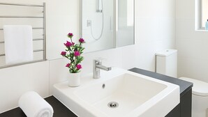 A modern bathroom with a large white sink, dark countertop, and a mirror above it. - Friendly Homestay - Ormiston, Auckland (Auckland)