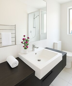 Ein modernes Badezimmer mit einem großen weißen Waschbecken, einer dunklen Arbeitsplatte und einem Spiegel darüber.