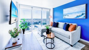 Una sala de estar moderna con un sofá, una mesa de centro y vistas a la ciudad a través de amplias ventanas.