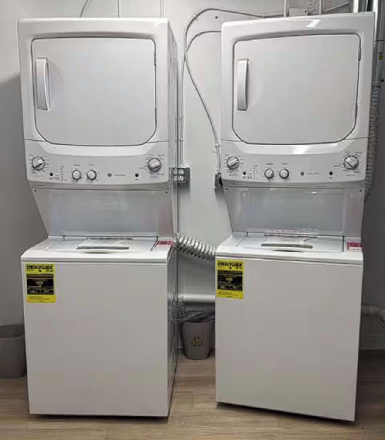 Two stacked washing machines with control panels and a trash bin.