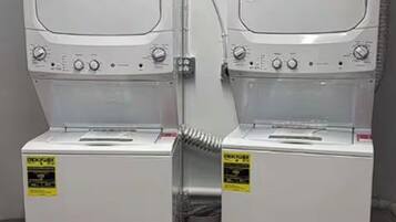 Two stacked washing machines with control panels and a trash bin.
