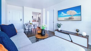 Una sala de estar moderna con un sofá, una mesa de centro, un televisor y un comedor al fondo.