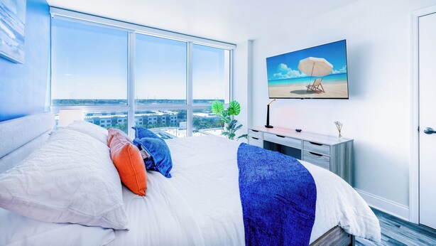 Un dormitorio con una cama grande, un televisor montado en la pared y vistas a la ciudad.