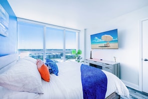 A bedroom with a large bed, a TV mounted on the wall, and a city view. - Luxury Downtown Fort Myers Apt/Pool View • King Bed • Walk to Dining/Nightlife (Fort Myers)