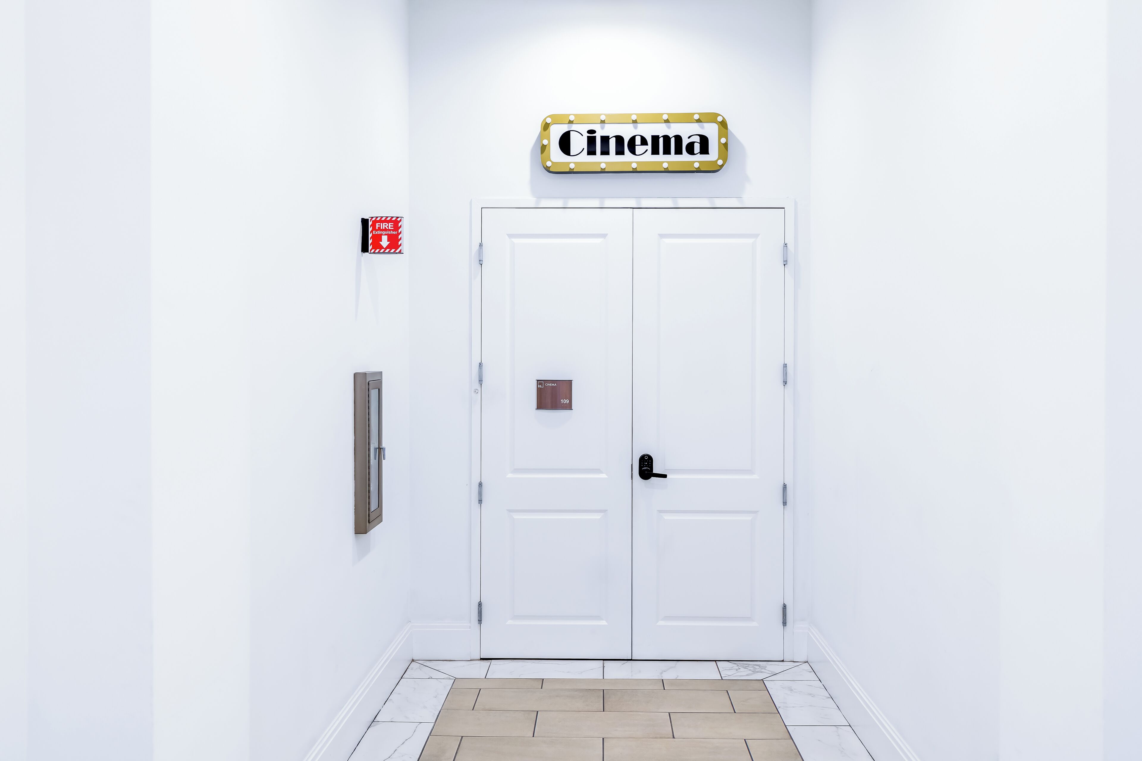 A white door with a 'Cinema' sign above it, a fire alarm, and a doorbell.