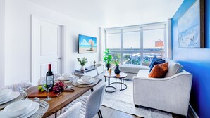 Un comedor con una mesa de madera dispuesta para una comida, un sofá y un amplio ventanal con vistas a la ciudad.