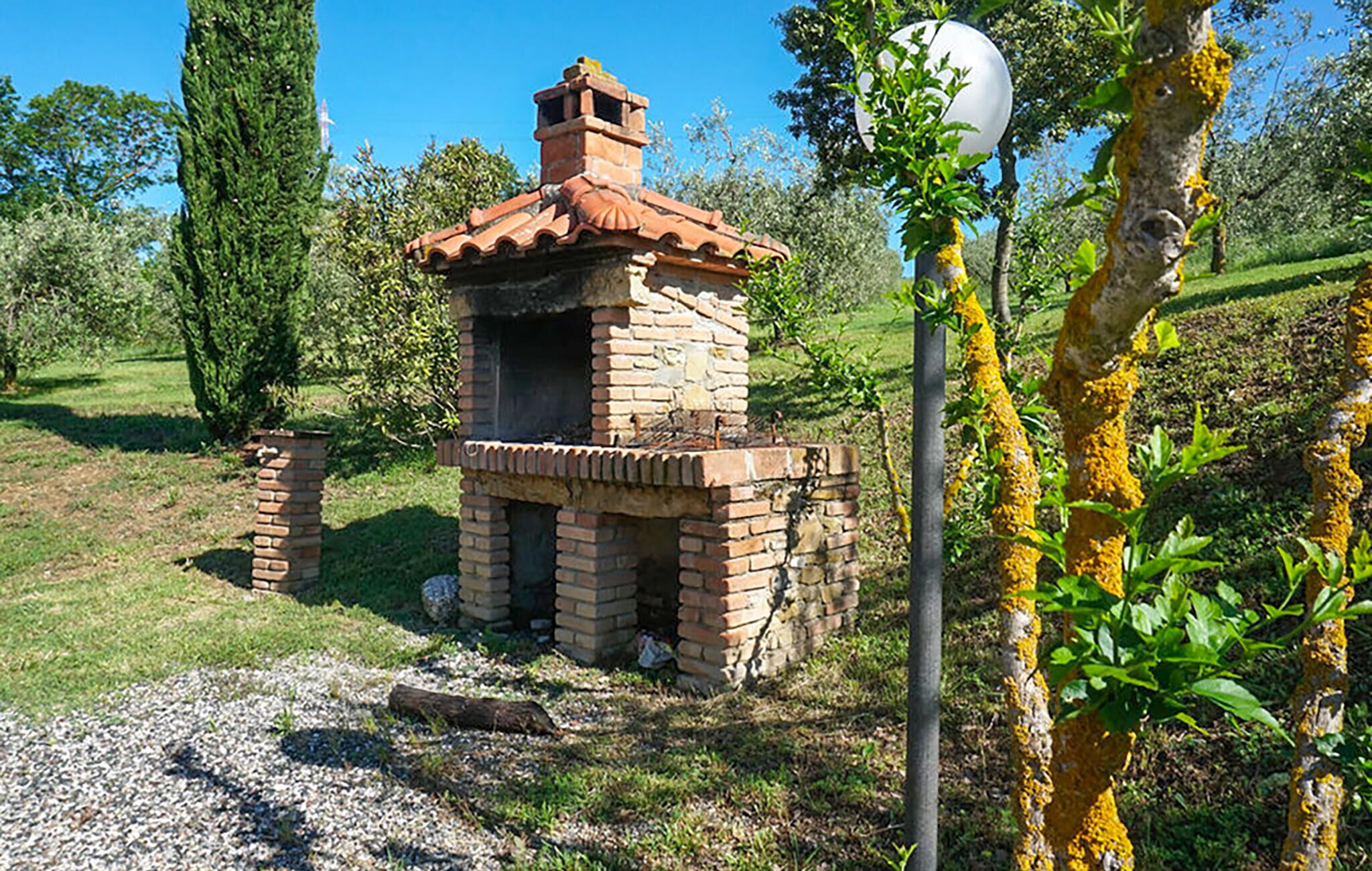 Une structure de four extérieur en briques, dotée d’une cheminée, entourée de verdure et d’arbres.