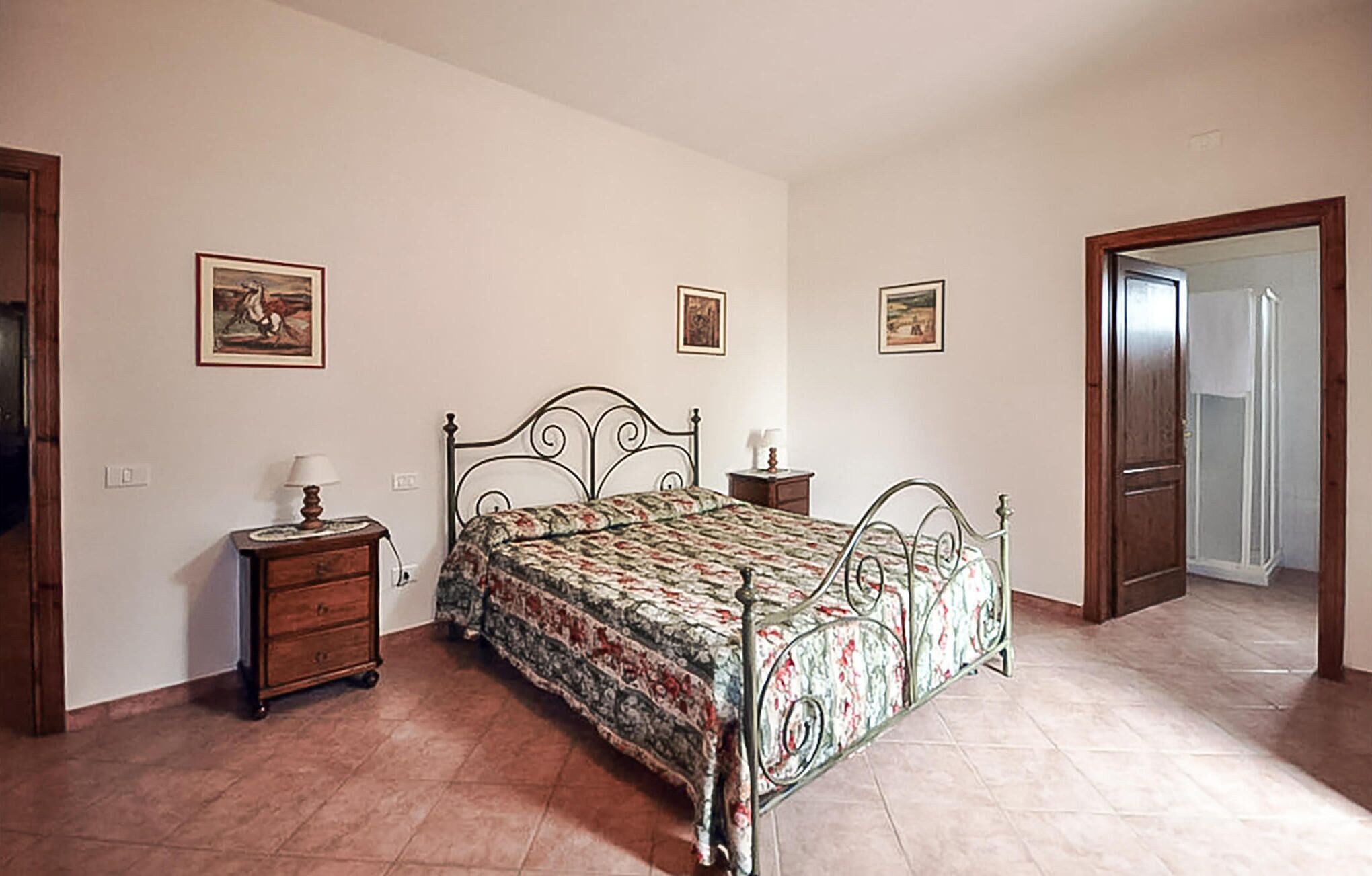 Een slaapkamer met een bed, nachtkastjes, een houten dressoir en een deur naar een andere kamer.