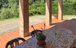 Eine Terrasse mit Tisch und Stühlen, umgeben von Ziegelstützen und Blick auf einen Garten.