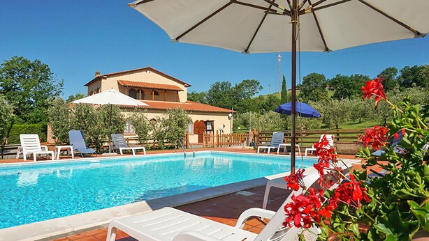 A pool area with lounge chairs and umbrellas, a building with a tiled roof, and a clear blue sky. - Stunning apartment in Montecatini Val di Cecina (Montecatini Val di Cecina)