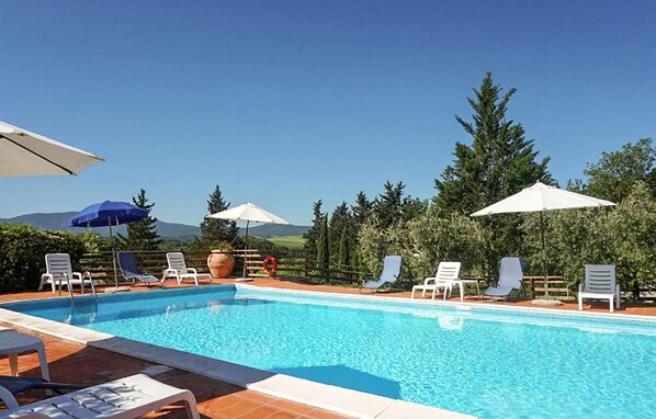 A swimming pool with lounge chairs and umbrellas, surrounded by trees and a clear sky. - Stunning home in Montecatini Val di Cecina (Montecatini Val di Cecina)