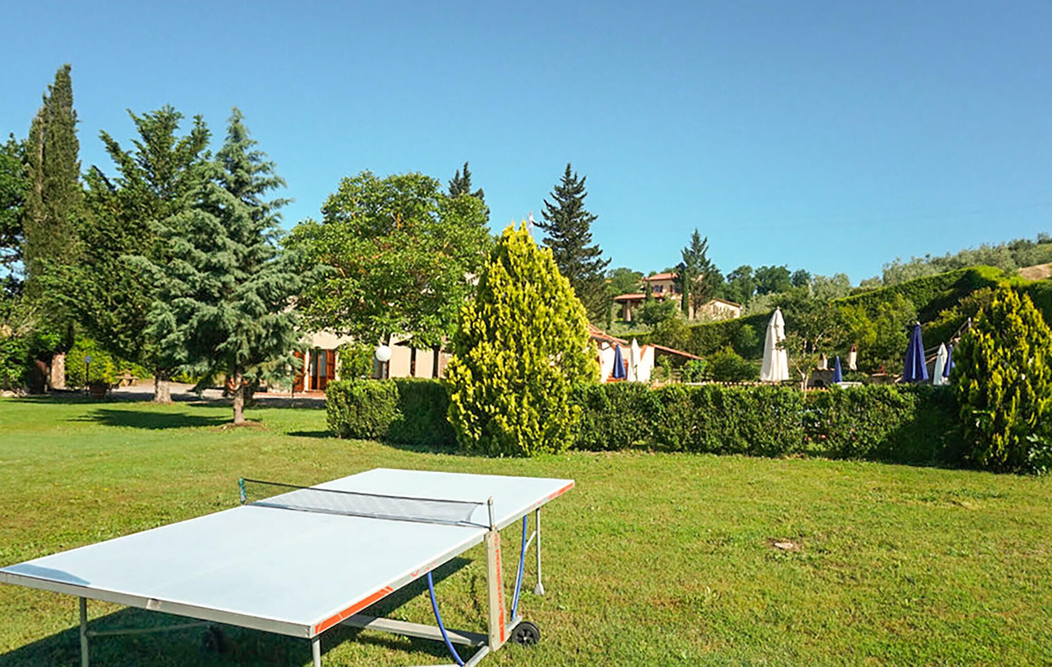 Un'area verde all'aperto con un tavolo da ping pong portatile, circondata da alberi e un edificio con tetto rosso.