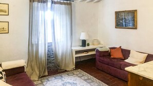 Un salon avec un canapé, une petite table avec une lampe, un tapis et une fenêtre avec des rideaux.