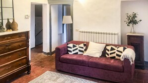 Une pièce avec un canapé violet, une commode en bois, un radiateur et une plante.