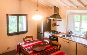 Eine Küche mit Herd, Spüle und Fenster. Ein Tisch mit Stühlen und einer Schüssel steht daneben.