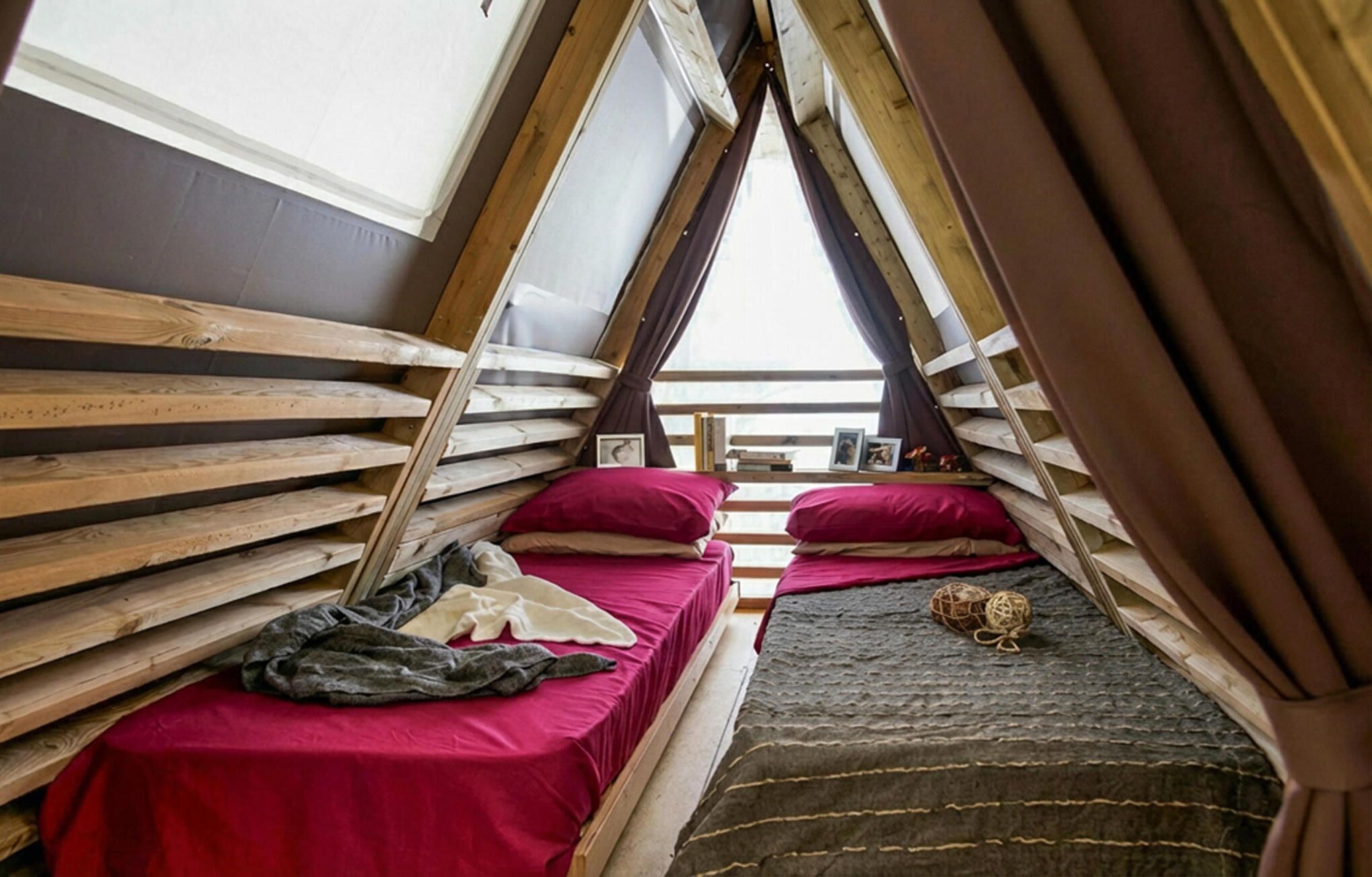 Un dormitorio ático pequeño y triangular con dos camas, una mesa y vistas al cielo.