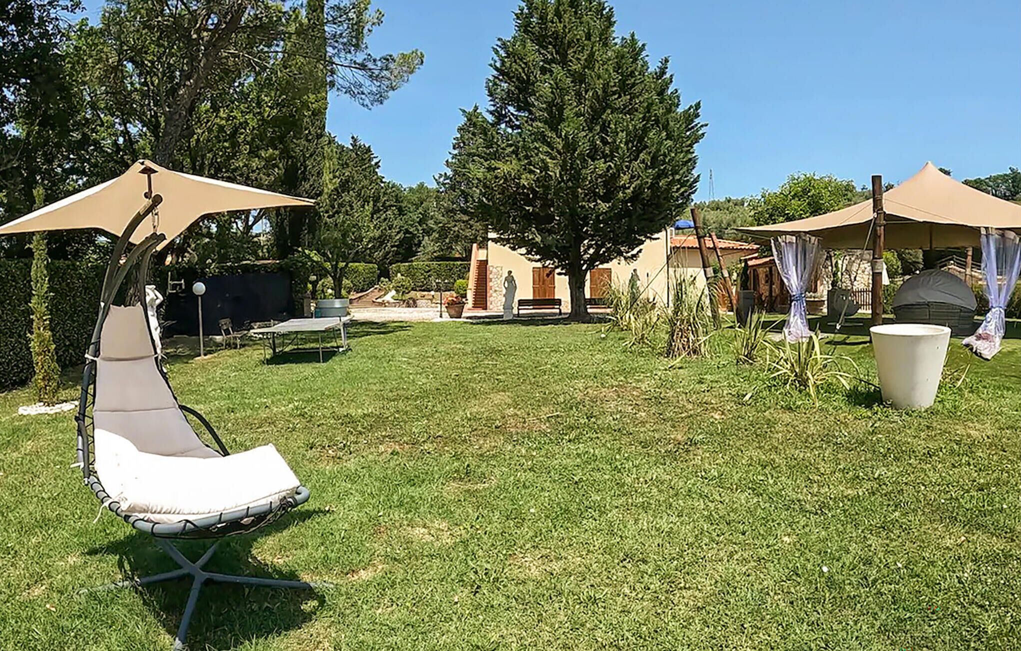 Un giardino sul retro con prato, una sedia a dondolo, un tavolo e due tende.