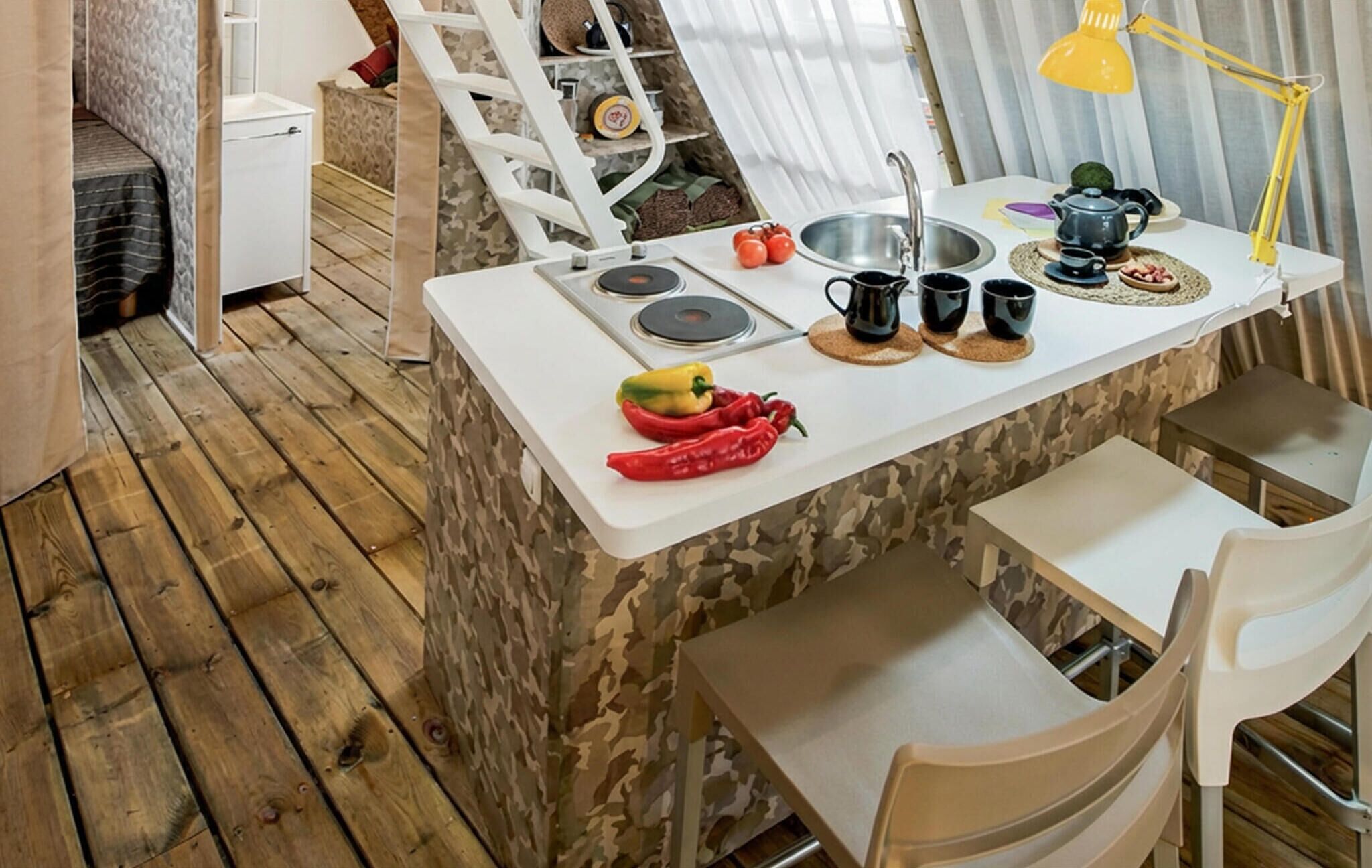 A compact kitchen with a white countertop, a sink, and a stove. There are two chairs and a small table.